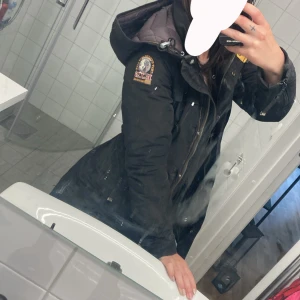 Svart Parajumpers parkajacka med huva - Gammal   Parajumpers model  med huva och parajumer loggan på ärmen. Jackan har dragkedja framtill, flera fickor och en gul detalj vid kragen. Perfekt för höst och vår jacka 