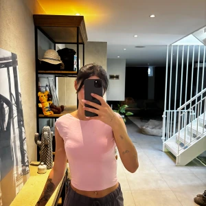 Ljusrosa croppad topp med öppen rygg - Säljer en ljusrosa croppad topp med korta ärmar och öppen rygg. Toppen har en tight passform och är tillverkad i ett mjukt bomullsmaterial. Perfekt för dig som gillar en enkel men ändå snygg look med en twist baktill.
