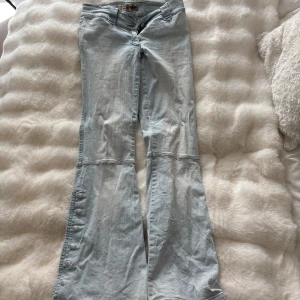 Ljusblå bootcut jeans med knappar - Säljer ett par ljusblå jeans från True Religion med bootcut och snygga knappar längs utsidan av benen. Jeansen har klassisk femficksdesign, bälteshällor och dragkedja. Perfekta för dig som gillar retrovibbar och vill sticka ut lite extra.