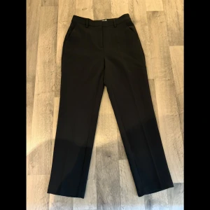 Kostymbyxor  - Klassiska svarta kostymbyxor från NA-KD i rak modell med pressveck och hällor för bälte. Byxorna har fickor fram och dekorfickor bak. Perfekta för en clean och stilren look.