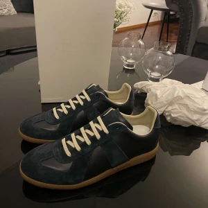 Mörkblå sneakers från Maison Margiela - Maison Margiela sneakers i mörkblå mocka och skinn med beige snörning och innersida. Klassisk gummisula i brunt och stilren design. Kvitto och box finns.