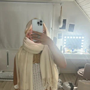Beige ullhalsduk från Acne Studios - Säljer en stor och lyxig beige halsduk från Acne Studios. Den är 200x70 cm, har fransar i kanterna och är tillverkad i mjuk ull. Halsduken är helt oanvänd, bara legat i min garderob då jag inte tycker den passar mig.