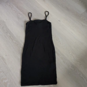 Svart tight kortklänning från Amisu - Svart tight kortklänning från Amisu i storlek 32. Klänningen har smala axelband och är tillverkad i mjuk bomull med lite stretch. Enkel och stilren modell som sitter snyggt på kroppen. Perfekt för dig som gillar minimalistisk stil.