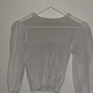 Vit spetsstickad tröja från Zara - Supersöt vit stickad tröja från Zara med genombrutet spetsmönster och puffiga långärmar. Tröjan har ribbade muddar och en feminin, lite romantisk vibe. Perfekt att styla med jeans eller kjol för en trendig look.