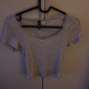 Grå croppad topp med spets från H&M - Säljer denna supersöta tröja från Hm med spets och rosett. Den är i storlek S och är använd fåtal gånger. 