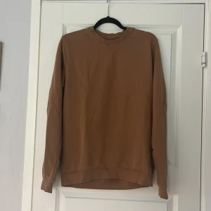 Brun sweatshirt från Dressmann M - En stilren brun sweatshirt från Dressmann i storlek M. Tröjan har rund halsringning, långa ärmar och ribbade muddar. Perfekt basic-plagg i mjuk bomull som funkar till många olika outfits.