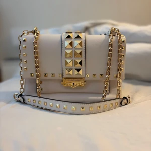 Vit och guld axelväska från Michael Kors - Säljer en snygg vit axelväska från Michael Kors med guldiga nitar och kedjedetaljer. Använd enstaka gång, sparsamt! 