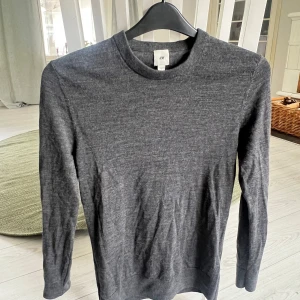 Stickad tröja  - En stilren mörkgrå långärmad tröja från H&M. Tröjan har rund halsringning och är tillverkad i mjuk bomullsmix som känns skön mot huden. Perfekt att bära som den är eller under en jacka. Enkel och clean look som funkar till det mesta.