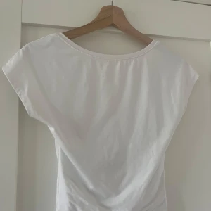 Vit topp med öppen rygg - Säljer en vit topp med korta ärmar och öppen rygg. T-shirten har en smickrande passform och är superenkel att styla. Använd ett fåtal gånger. Från bikbok storlek XS men passar även S