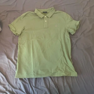 Ljusgrön pikétröja från GANT - Snygg ljusgrön pikétröja från GANT i klassisk modell med krage och två knappar framtill. Tröjan har korta ärmar och liten broderad logga på bröstet. Perfekt för en fräsch och avslappnad stil under varmare dagar.