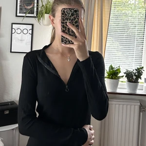 Svart ribbad kortklänning med zip - Svart ribbad klänning med lång ärm och halv dragkedja framtill. Tight passform som framhäver figuren och kort längd. Perfekt för dig som gillar en stilren och enkel look. Materialet känns mjukt och stretchigt.