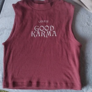 Vinröd ribbad linnetopp House Brand - Vinröd ribbad linnetopp från House Brand med trycket 'Create Good Karma' framtill. Toppen är ärmlös och croppad, perfekt för en chill och trendig look. Mjuk och stretchig bomullskänsla som sitter snyggt på kroppen.