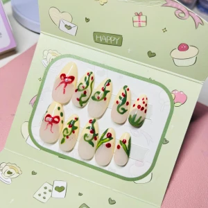 Press on-naglar med röd och grön design - Snygga press on-naglar i mandelform med ljusgul bas, dekorerade med handmålade röda rosetter, gröna slingor och röda prickar. Perfekt för dig som vill ha en lekfull och färgglad look. Kommer i söt förpackning och är enkla att applicera.
