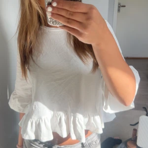 Vit blus med volangdetalj - Supersöt vit blus med volang längst ner och vida trekvartsärmar. Den är croppad och har en luftig passform som känns riktigt fräsch till jeans eller kjol. Perfekt för vår och sommar när du vill ha något lätt och stilrent.
