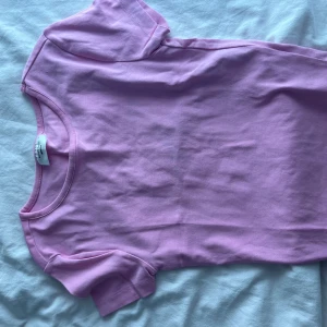 Ljusrosa t-shirt från Gina Tricot - En basic ljusrosa t-shirt från Gina Tricot med rund halsringning och korta ärmar. Modellen är enkel och passar perfekt till jeans eller kjol. Tillverkad i mjuk bomull för en skön känsla hela dagen.