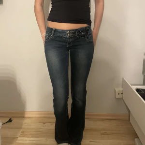 Lågmidjade jeans med rosett! - Snygga mörkblå jeans med bootcut passform och låg midja. Jeans är utsydda hemma så vi kan inte garantera att allt är 100% perfekt. Men den ser ut exakt som bilderna! MÅTT PÅ TREDJE BILDEN!!!! VI SKICKAR INGS FLER BILDER!