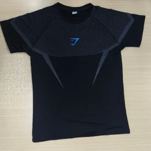 Gymshark onyx 5.0 blå - Svart t-shirt från Gymshark med gråa grafiska detaljer och blå logga på bröstet. Det är gymshark onyx settet som är slutsålt över allt och kommer ej komma tillbaka. Helt ny.