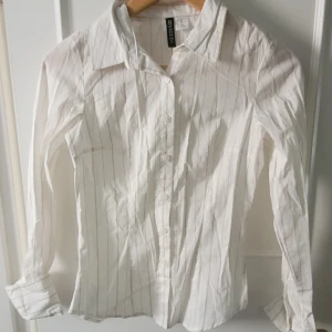Dam skjorta från H&M - Klassisk vit skjorta från H&M Divided med mörk beige linjer i storlek XXS men passar även XS. Det är en figurnära med klassisk vikbar krage likaså vikbara ärmar.