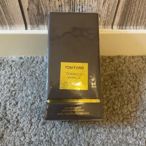 Tom Ford Tobacco Vanille EdP 100ml - Tom Ford Tobacco Vanille Eau de Parfum 100 ml. Lyxig parfym i mörkbrun, rektangulär kartong med gulddetaljer. Doften kombinerar varma toner av tobak och vanilj för en djup och elegant känsla. Perfekt för dig som gillar exklusiva och kryddiga dofter.