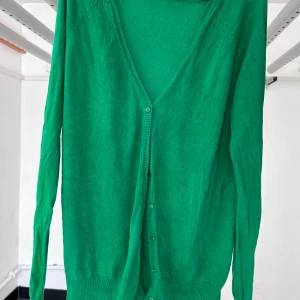 Grön kofta från Zara - Säljer en tunn grön kofta från Zara med v-ringning och knäppning framtill. Koftan har långa ärmar och är tillverkad i en mjuk bomulls- och nylonblandning. Perfekt att slänga över en topp eller klänning.