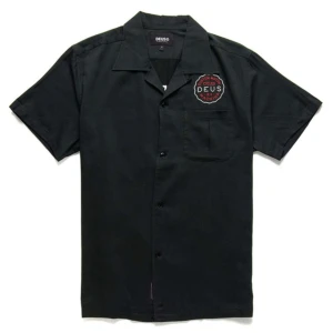 Svart kortärmad skjorta från Deus Ex Machina - Svart skjorta med kort ärm från Deus Ex Machina. Skjortan har broderad logga på bröstet och stort tryck på ryggen. Klassisk krage och knäppning framtill. Perfekt för en avslappnad och cool stil.