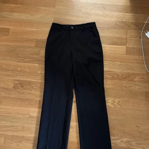 Svarta kostymbyxor med raka ben - Säljer ett par klassiska svarta kostymbyxor med raka ben och pressveck. Byxorna har hällor för bälte, knapp och dragkedja. Byxorna är knappast inte använda kanske bara 1-2 gånger skulle jag tro, Perfekta till vad som helst för outfit🥰, kontakta mig om ni är sugna på att köpa ☺️