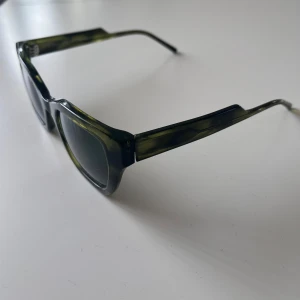 Gröna solglasögon från Kaibosh - Snygga solglasögon från Kaibosh i en transparent grön färg med markerad båge och svarta glas. Modellen har en kantig form och ger en cool look✅Perfekta för soliga dagar och en stilren accessoar till din outfit🔥