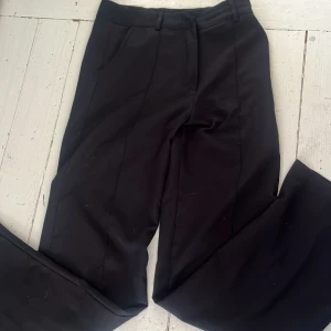 Svarta kostymbyxor med pressveck - Snygga svarta kostymbyxor med klassiskt snitt och pressveck framtill. Byxorna har normal passform, hällor för bälte och sidofickor. Perfekta för en stilren look.