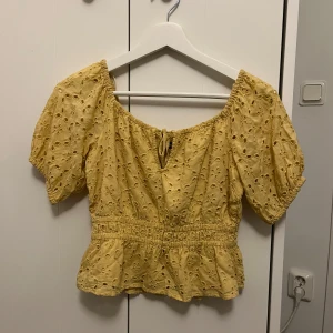Gul blommig blus med volang och knyt - Söt gul blus med broderade blommor, volang nertill och indragen midja. Puffiga korta ärmar och knytning fram vid halsen. Perfekt till sommaren! Storlek xs men skulle även säga att den passar s då den är stretchig.
