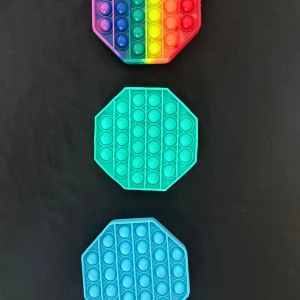 Tre pop it-leksaker i olika färger - Säljer tre pop it-leksaker i silikon. En är regnbågsfärgad med åtta kanter, en är turkos och en är ljusblå, båda med åtta kanter. Perfekt för att stressa ner eller bara ha kul med kompisar.
