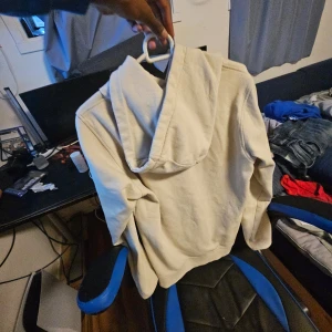 Beige hoodie från Fila - Säljer en beige hoodie från Fila med stor logga framtill. Tröjan har huva och en klassisk känguruficka. Perfekt för en avslappnad stil.