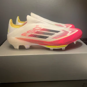 Adidas f50+ - Säljer ett par Adidas X Speedportal+ fotbollsskor i vitt med röda och svarta detaljer. Skorna har en strömlinjeformad design utan snörning och är tillverkade i syntetmaterial. Perfekta för dig som vill ha lättviktsskor med bra grepp på planen.