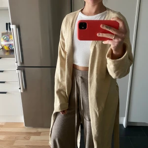 Beige cardigan  från NA-KD - Beige cardigan  från NA-KD i storlek XS. Lång ärm, öppen front och ett matchande bälte i midjan. Perfekt för lager-på-lager och enkel att styla till olika outfits!