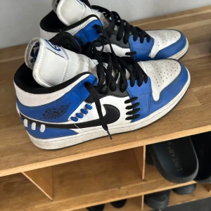 Nike Air Jordans i blått och vitt - Säljer ett par Nike Air Jordans med blå, vit och svarta detaljer. Skorna har svart snörning, perforerad tå och klassisk Nike-logga på sidan. Perfekta för dig som gillar streetwear och vill sticka ut med färg.