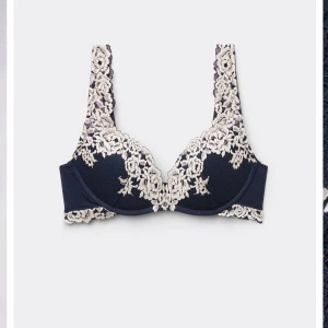 Mörkblå bh med spetsdetaljer - Snygg mörkblå bh med dekorativa spetsdetaljer i beige längs kupor och axelband. Ger en elegant och feminin känsla med vackert blommönster i spetsen. Perfekt för dig som vill ha något extra fint under kläderna. Men vill att ni ska vara medvetna om att jag själv köpt den på Plick då användaren sa att den va 70b så jag utgår från de men den är lite större