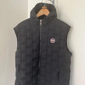 Svart dunväst från Colmar - Snygg svart dunväst från Colmar med quiltad design och dragkedja framtill. Västen har huva och två fickor med dragkedja. Perfekt för lager-på-lager och stilren look.