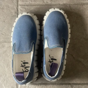 Eytys Blå Sneaker - Säljer ett par blå slip-on sneakers med kraftig, vit och räfflad sula. Skorna har en enkel och stilren design i textilmaterial. Dem är inte användna mer än 2-3 gånger, säljer då de inte kommer till användning. Pris är diskuterbart 