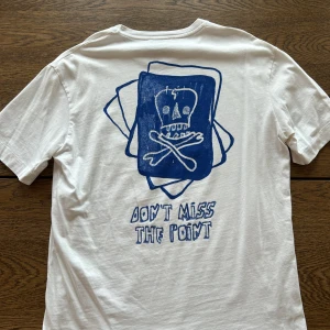 Vit t-shirt med blått tryck från ZARA - Vit t-shirt från ZARA med blått tryck av dödskalle och korslagda ben på bröstet och stort motiv på ryggen med texten 'Don't miss the point'. Klassisk passform och rund halsringning. Storlek Medium, sparsamt använd.
