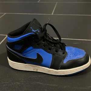 Nike Air Jordans svart/blå - Säljer ett par Nike Air Jordans i svart och blått med vit sula. Skorna har klassisk hög modell, svart snörning och rund tå. Perfekta för dig som gillar streetwear och vill sticka ut med en ikonisk sneaker.