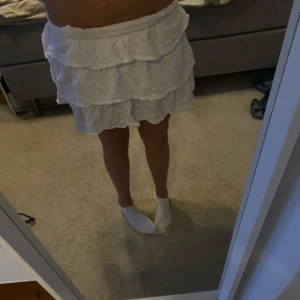 Vit volangkjol från NA-KD - Superfin vit kortkjol från NA-KD med broderade blommor och flera volanger. Kjolen har en romantisk känsla och är perfekt för varma dagar. Resår i midjan för extra komfort.