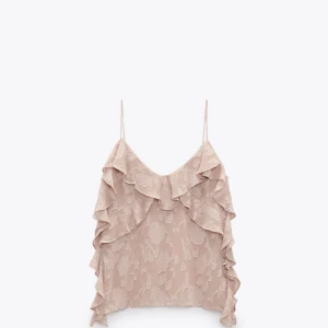 Rosa volangprydd linnetopp med spetsdetaljer - Säljer en söt rosa topp med tunna axelband och volanger längs fram- och sidorna. Toppen har ett diskret blommönster i spets och är aldrig använd.