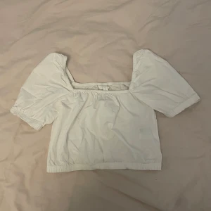 Vit croppad topp med puffärmar - Säljer en söt vit croppad topp med bred resår i nederkant och vid halsen. Toppen har korta puffärmar och en fyrkantig urringning. Perfekt att styla med jeans eller kjol.