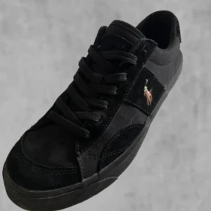 Svarta sneakers från Polo Ralph Lauren - Svarta sneakers med låg profil och rund tå från Polo Ralph Lauren. Skorna har snörning och är tillverkade i mocka och syntet, med den klassiska broderade Polo-loggan på sidan. Perfekta för en stilren och avslappnad look.