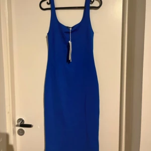 Marinblå tight klänning från Zara - Säljer en marinblå tight klänning från Zara med smala axelband och djup urringning. Klänningen är figurnära och har en slits bak för extra rörelsefrihet. Perfekt för dig som vill sticka ut med en färgstark look.