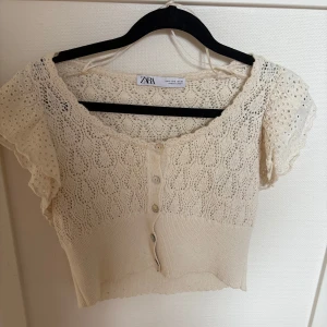 Vit spetsblus med knappar från Zara - Säljer en söt vit blus från Zara med spetsdetaljer och korta volangärmar. Blusen har knappar framtill och är lite croppad.
