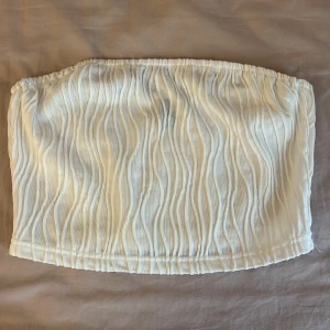 Vit plisserad tubtopp - Säljer en vit tubtopp med plisserad struktur och vågigt mönster. Toppen är elastisk upptill och nertill för bra passform. Perfekt att styla till sommarens outfits!