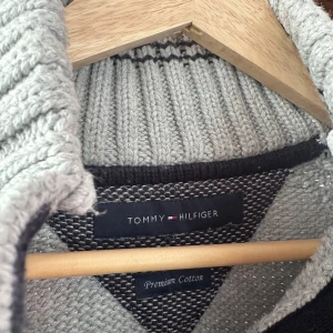 Ljusgrå stickad tröja med knappar från Tommy Hilfiger - Säljer en ljusgrå stickad tröja från Tommy Hilfiger i premium bomull. Tröjan har hög krage med fyra bruna knappar och diskret logga på bröstet. Perfekt för dig som gillar klassisk och stilren design. Storlek M