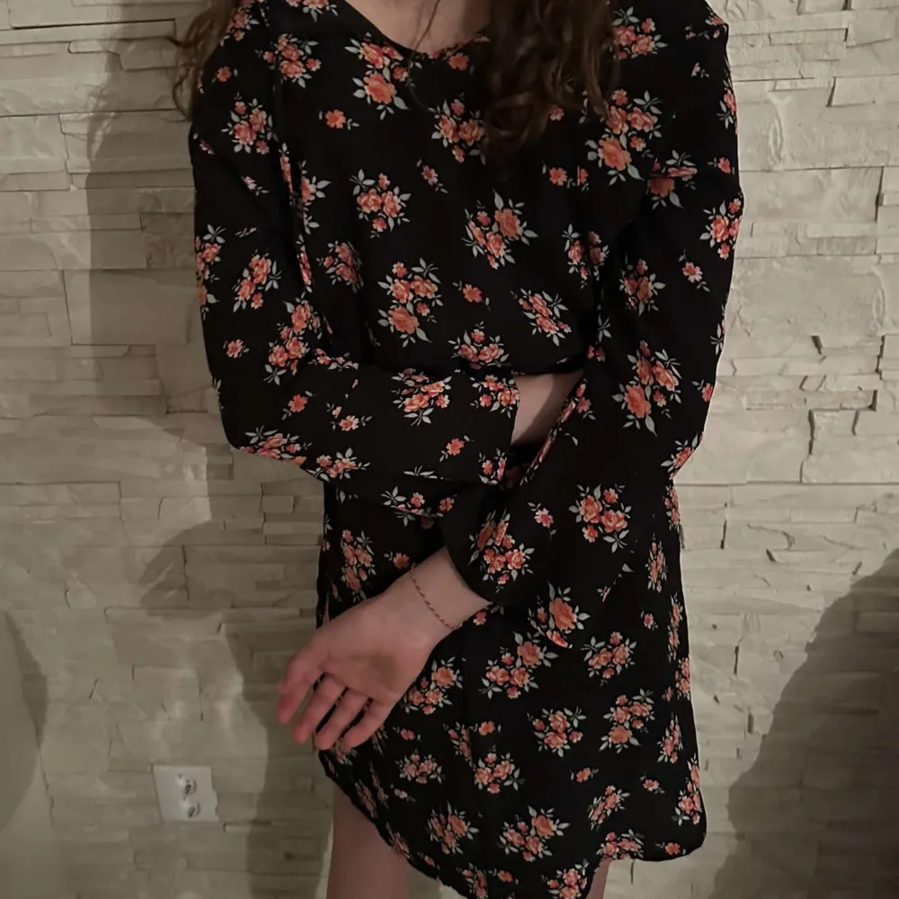 Säljer en svart klänning med små blommiga mönster i rött och rosa. Klänningen har långa ärmar och en avslappnad passform med resår i midjan. Perfekt för dig som gillar romantiska och feminina plagg. Pris kan diskuteras.. Mekot.
