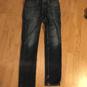 Mörkblå jeans från Hollister - Snygga mörkblå jeans från Hollister med klassisk femficksdesign och raka ben. Jeansen har diskreta slitningar och kontrastsömmar, samt läderpatch med logga bak i midjan. Perfekta för en avslappnad stil.
