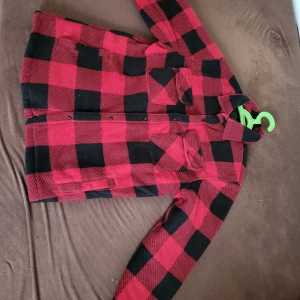Röd och svart rutig Skjort Jacka - Säljer en röd och svart rutig overshirt med klassisk krage och knappar framtill. Jackan har två bröstfickor med lock och knapp samt två sidofickor. Perfekt för lager-på-lager och ger en cool, avslappnad stil. Nästan helt ny! Har bara haft den på mig ett par gånger.
